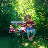 Una bambina seduta in giardino su una sedia da giardino e tra le braccia una bambola Nanchen con un vestito blu e capelli biondi.