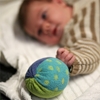A baby is laying down looking at Nanchen's soft blue-green terry cloth rattle ball.